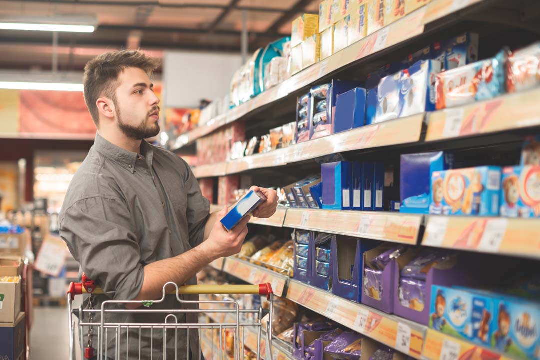 Man stands in a supermarket with a bundle of biscuits in his hands and looks at the shelf with sweets. The buyer buys cookies in a supermarket, looking at packaging with sweet Tillmann Branche Lebensmittel