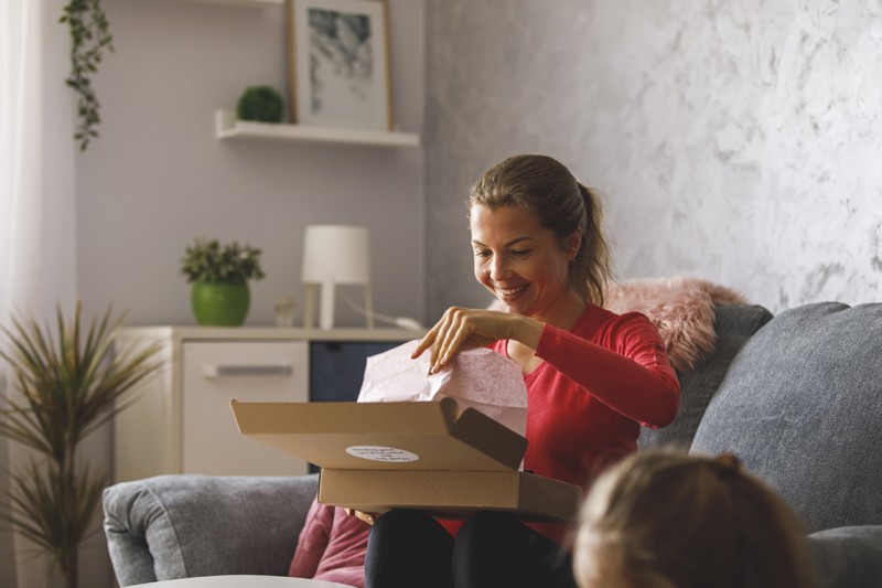 Frau sitzt auf einer Couch und öffnet ein Paket aus dem Online Versandhandel